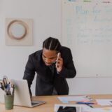 man with braided hair leaning over desk talking on phone