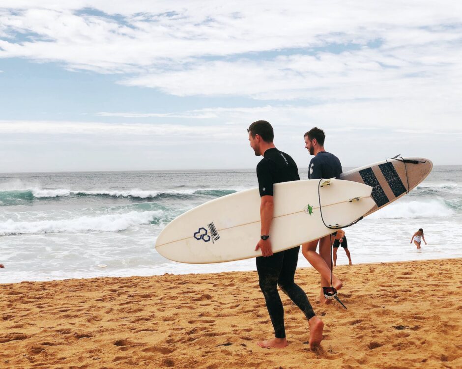 two men carrying surfboards near seashore