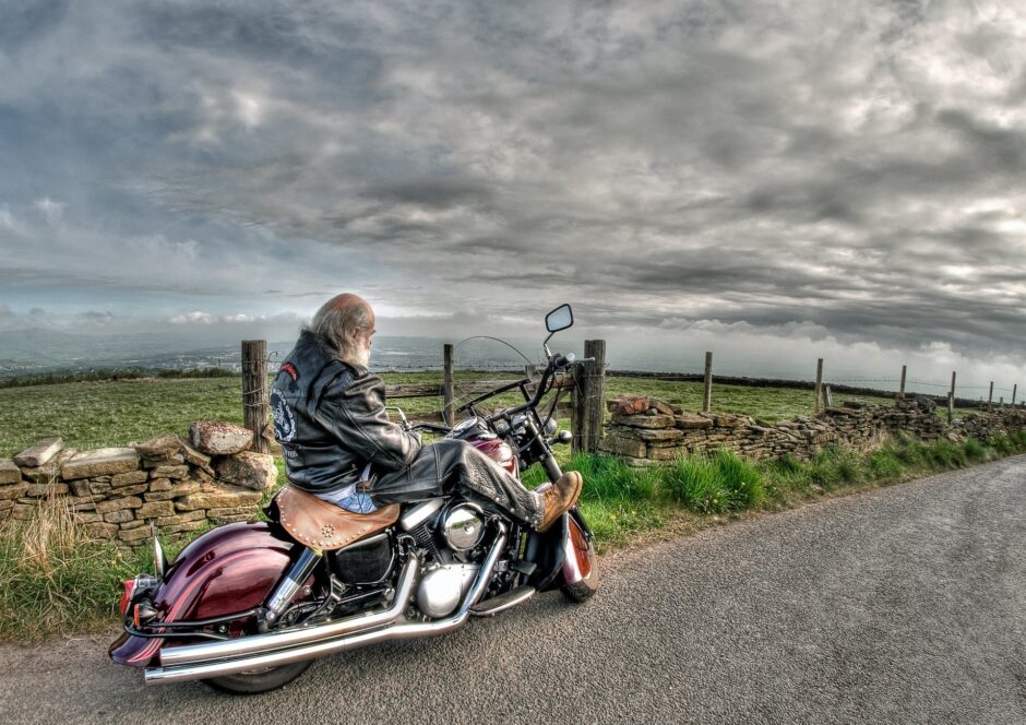 man wearing black leather jacket riding cruiser motorcycle on road