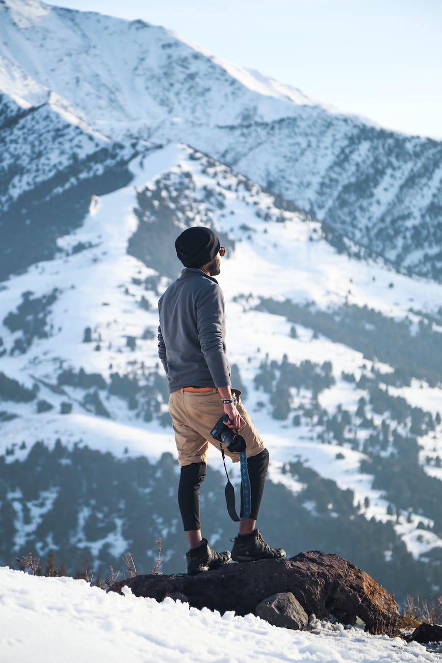 man wearing gray long sleeved shirt and brown shorts holding black dslr camera on mountain