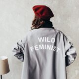 woman wearing red beret and gray long sleeve dress with wild feminist print