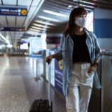 woman with a face mask holding her luggage