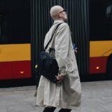 man in beige coat walking beside a bus