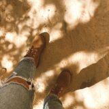 a person s legs in jeans and boots standing in the sand