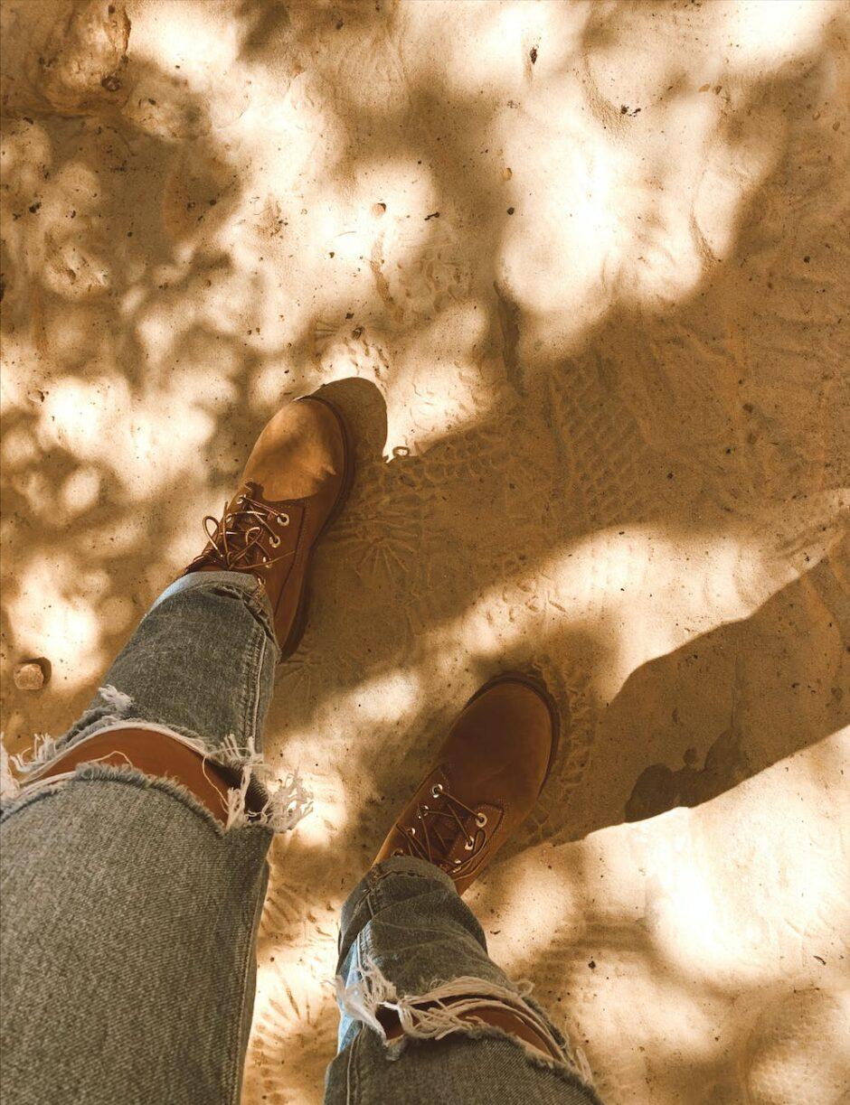 a person s legs in jeans and boots standing in the sand