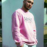 man in pink sweater posing with a wall in background