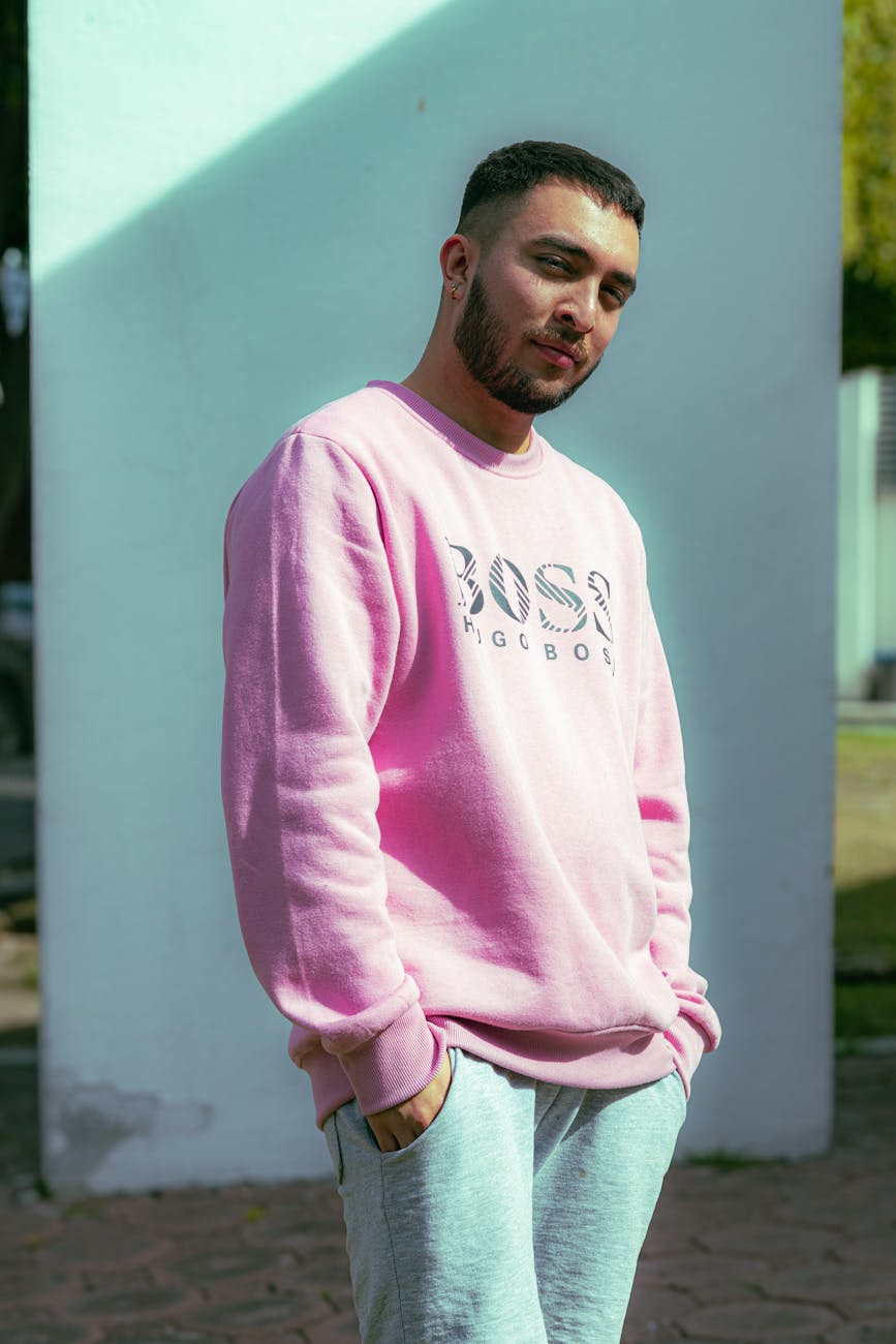 man in pink sweater posing with a wall in background