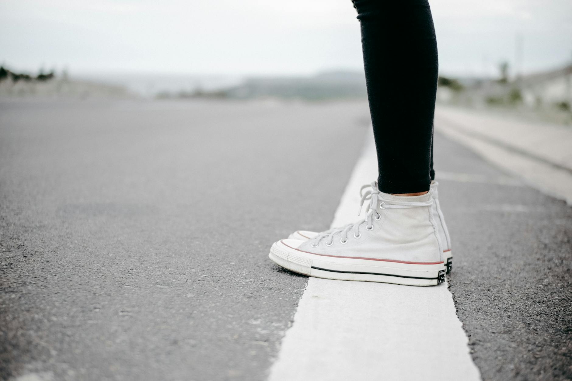 person wearing white high top lace up sneakers standing on white line