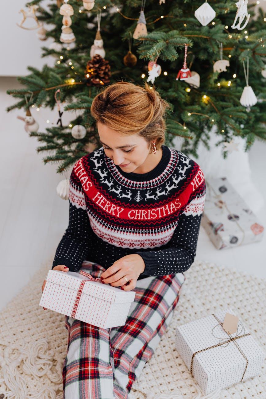 woman sitting next to a christmas tree and unboxing a present