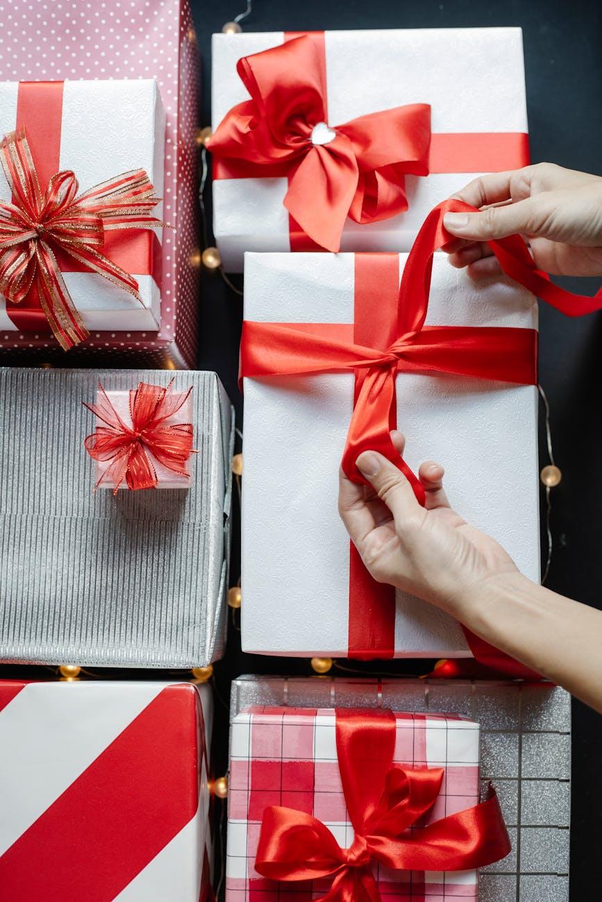 crop person tying ribbon on gift box on christmas day