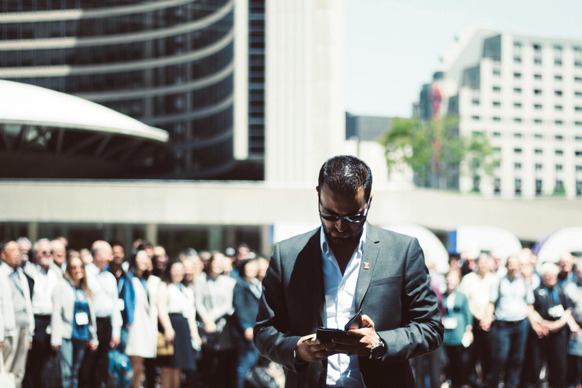 selective focus photography of man holding smartphone while standing near people
